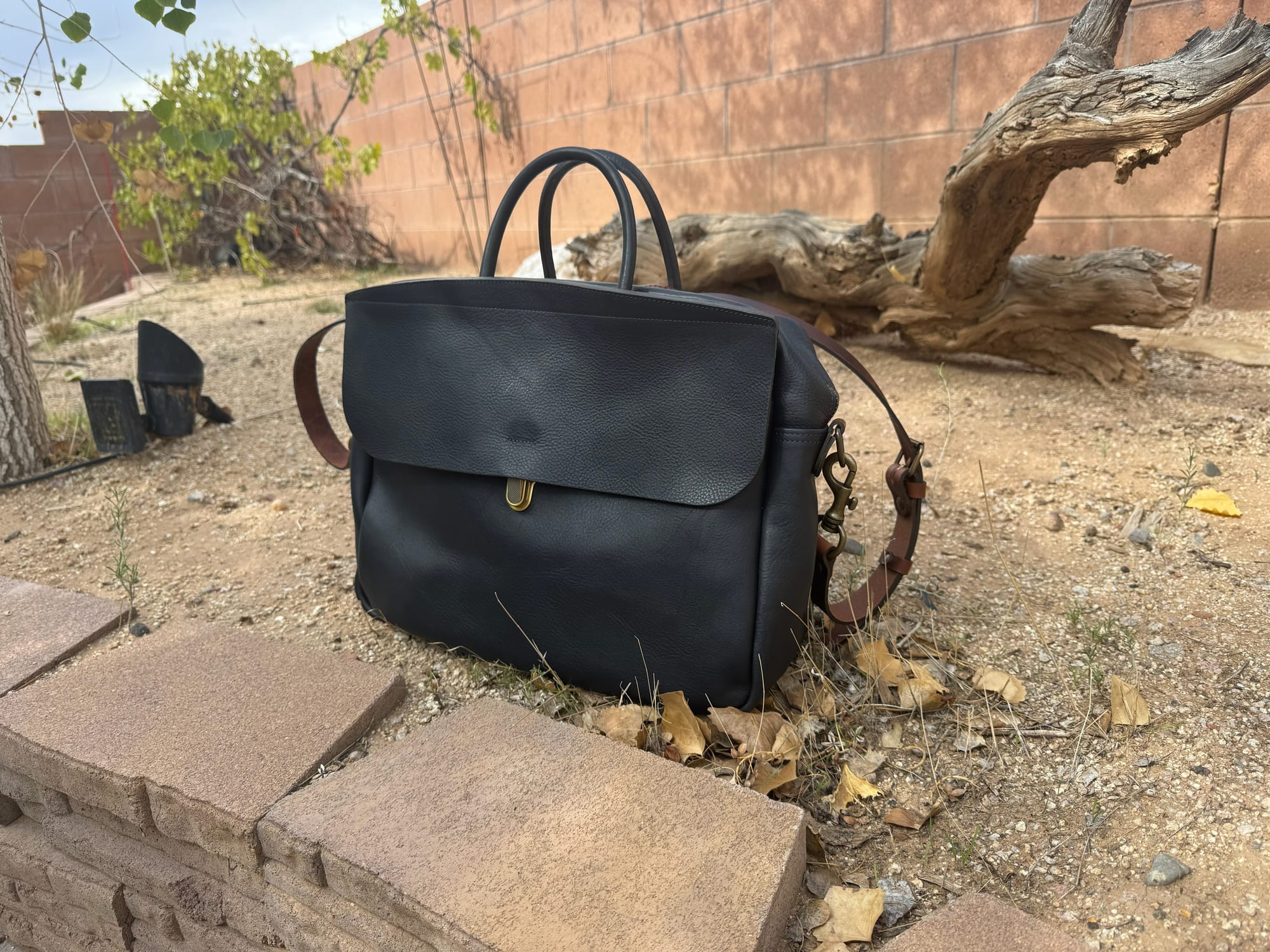 A navy-colored leather messenger bag sitting in nature