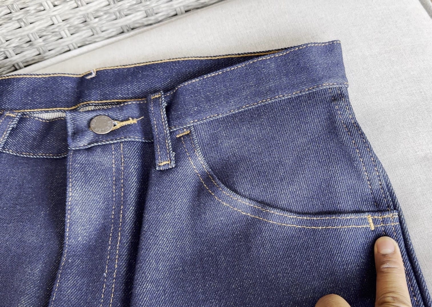 Pointing at a stitched bar tack where jeans are typically riveted with metal
